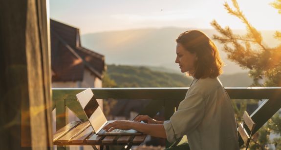 Frau sitzt mit Laptop auf dem Balkon